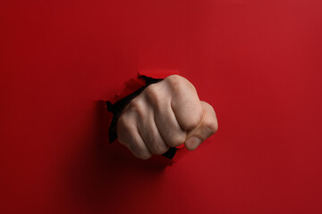 Man breaking through red paper with fist, closeup