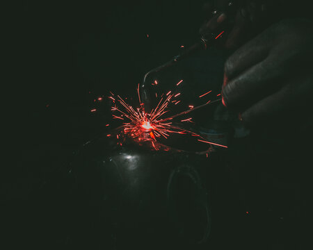 Closeup of a man welding a metal ball in the darkness
