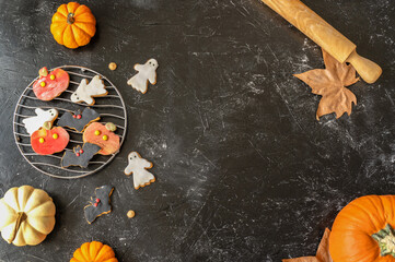 Halloween cookies on the black background with pumpkins and rolling pin