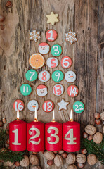 Burning candle on wooden background with 4th advent and homemade decorated gingerbread and fir tree. Postcard and Christmas background.