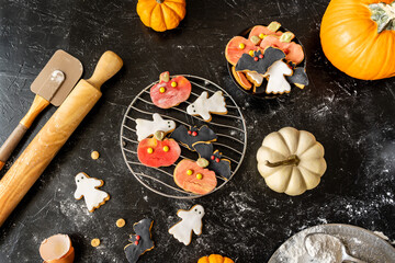 Halloween cookies on the black background with pumpkins, rolling pin, flour, beaten egg