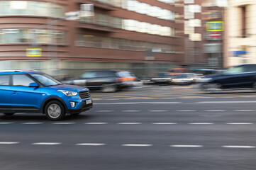 Fototapeta na wymiar Fast moving blue car on a city street. Blurred motion.