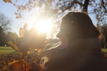 a young slender girl in a beige down jacket collects autumn fallen yellow leaves in the park on an...