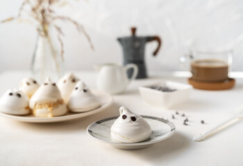 Meringues in a form of ghosts with cup of coffee, milk jar, chocolate drops and coffe pot on the light background
