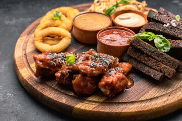 Beer snack on a wooden board. Onion rings, croutons, squid, grilled chicken wings and sauces