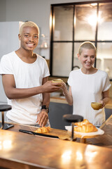 Fototapeta na wymiar Multiracial couple drinking and toasting drink at home kitchen. Concept of relationship. Idea of modern domestic lifestyle. Black man and european girl spending time together in modern flat