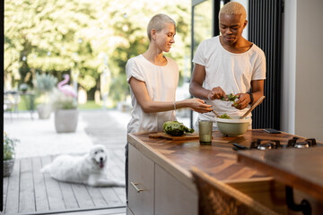 Fototapeta na wymiar Multiracial couple cooking salad together at home kitchen. Idea of healthy eating. Concept of relationship. Modern domestic lifestyle. Black man and european girl spending time together