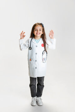 Full-length portrait of cute beautiful little girl, child in image of doctor wearing white lab coat posing isolated on white studio background