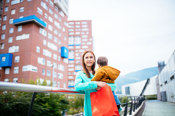 young adult woman talking carrying her baby around the city with colorful shopping bags