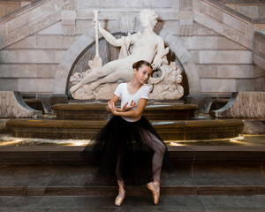 Pretty little girl posing in a ballerina costume in front of a 1750 French statue of goddess of the...