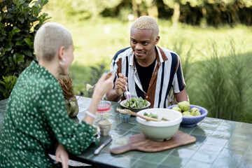 Multiracial couple eating organic food at dinner outdoors. Concept of relationship. Idea of healthy eating. Modern domestic lifestyle. Black man and european woman enjoying time together