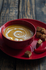 red plate with pumpkin soup and hot pepper on a dark background