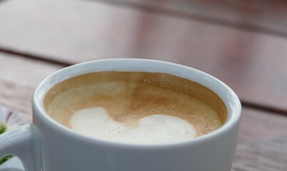 Coffee with creamy foam and white cup on wooden table