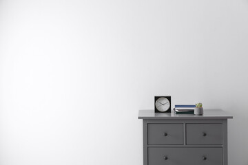 Books, houseplant and clock on chest of drawers near white wall indoors, space for text. Interior design