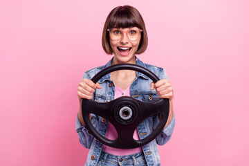 Portrait of attractive cheerful amazed girl holding steering having fun isolated over pink pastel color background