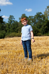 Naklejka na ściany i meble a red-haired boy stands on a golden straw stack