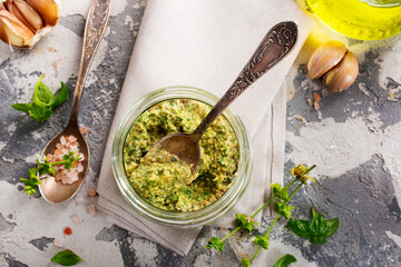 Homemade parsley pesto sauce and ingredients on dark cement background. Close up wiev of basil pesto in glass jar with ingredients.