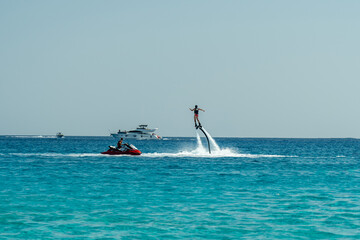 Fototapeta na wymiar Man flyboarding above the clear sea. Water sports adventure