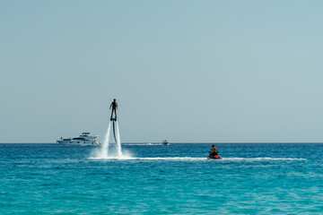 Man flyboarding above the clear sea. Water sports adventure