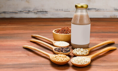 Fresh organic fruit extract drink in glass bottle beside wooden spoon of natural cereal grains, bean ingredient, and bowl of brown rice