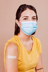 Portrait of a young female wearing protective mask after receiving a vaccine. Woman showing her bandaged arm after receiving vaccination.