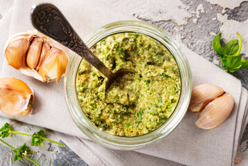 Homemade parsley pesto sauce and ingredients on dark cement background. Close up wiev of basil pesto in glass jar with ingredients.