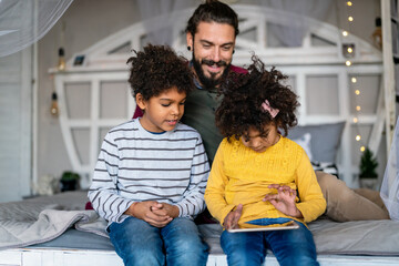 Happy father and children playing with digital tablet. Multiethnic family fun technology concept