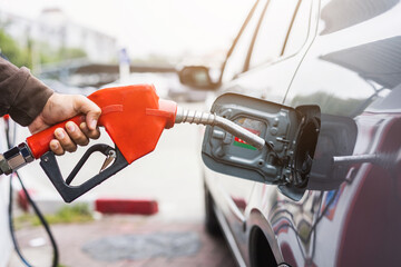 A gas station worker holds a fuel dispenser to fill the car with fuel. A young man's hand holds a...