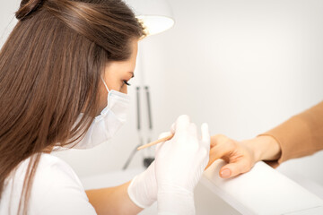 Fototapeta na wymiar Manicure master in protective face mask and white gloves apply polish to female fingernails