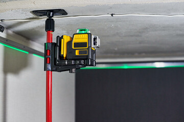Laser level measuring tool with visible green laser beam on wall of unfinished apartment