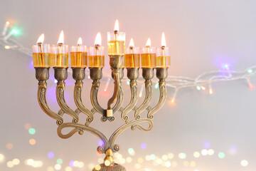 Image of jewish holiday Hanukkah with menorah (traditional candelabra) and oil candles over garland glitter lights background