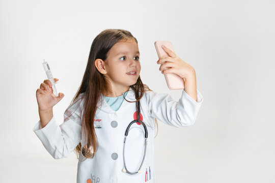 Close-up portrait of cute little girl, child in image of doctor wearing white lab coat with stethoscope isolated on white studio background