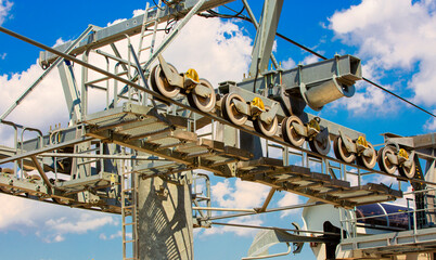 Close-up of a ski lift and traction wheels, on blue sky with clouds.