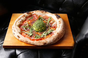 Pizza with Parma ham, arugula, and burrata cheese with green pesto.
A tasty dish.Culinary photography. Suggestion to serve the dish.
