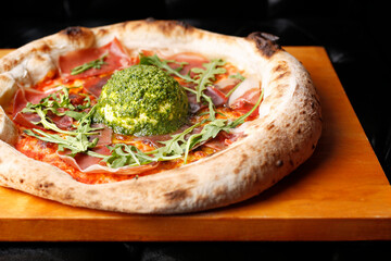 Pizza with Parma ham, arugula, and burrata cheese with green pesto.
A tasty dish.Culinary photography. Suggestion to serve the dish.
