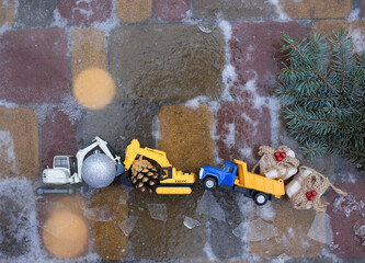 toy excavators, dump truck with Christmas decorations on icy paving slabs. preparation for new year...