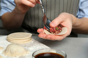 Woman putting gyoza filling in center of dough wrapper at light grey table, closeup