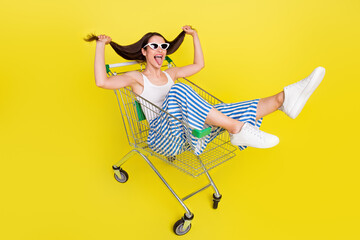 Full size photo of cool brunette lady sit in trunk tongue out wear top pants spactacles isolated on yellow color background