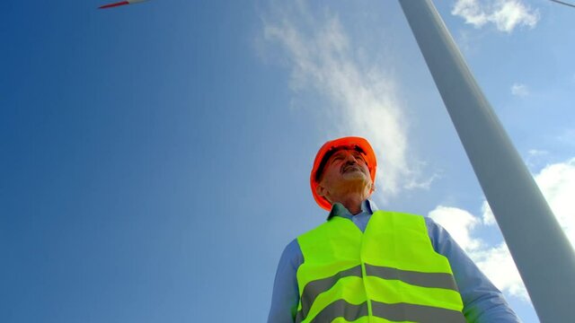 Wind Driven Generator Produces Alternative Energy. Engineer With Tablet Looks At Built Offshore Windmill Station Under Blue Sky Low Angle Shot