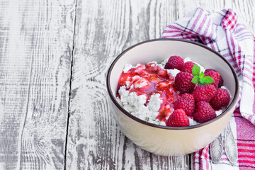Cottage cheese with raspberry in ceramic bowl on white wooden table