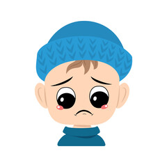 Boy with crying and tears emotion, sad face, depressive eyes in blue knitted hat. Cute kid with melancholy expression in autumnal or winter headdress. Head of adorable toddler