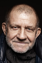 Close-up studio portrait of elderly man with gray stubble. He looks at the camera and smiles