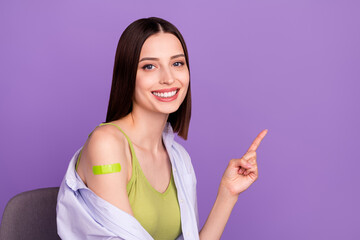 Photo of optimistic brunette millennial lady indicate empty space did vaccination wear top shirt isolated on purple background