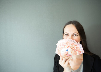 young woman covering her face with fan of euro money over grey background
