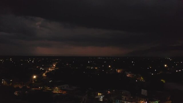 Aerial panoramic footage of modestly illuminated streets in night town. Heavy clouds and storm with lightning in distance. Valladolid, Mexico