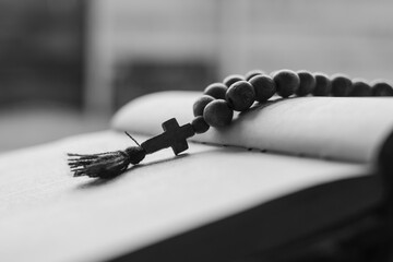 Wooden prayer beads with a Christian cross lie on the holy bible book on a wooden background. The concept of the Catholic and Orthodox faith.  Black and white photography
