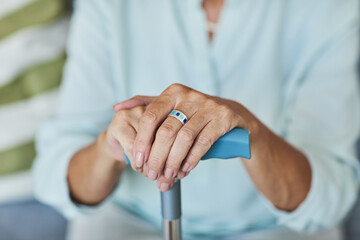 Close up of unrecognizable senior woman holding cane, focus on elegant hands with ring, copy space