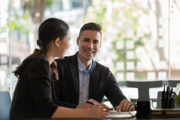 Multiethnic male caucasian mentor and female asian sitting at desk with laptop doing paperwork...