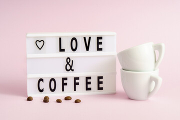 Love and coffee spelled in letters on lightbox with coffee beans and couple of cups on pink...