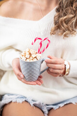 Girl in knitted wool sweater is holding a mug with hot chocolate with marshmallow.